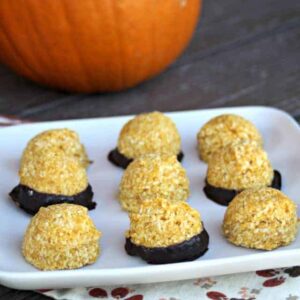 A white plate holds eight coconut macaroons partially dipped in chocolate, arranged in two rows. A pumpkin is visible in the background, creating a cozy setting perfect for exploring tapioca flour recipes.