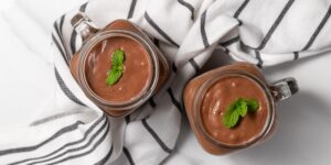 Two glass mugs of chocolate mousse, perfect for vegetarian keto recipes, garnished with mint leaves and placed on a white napkin with black stripes.