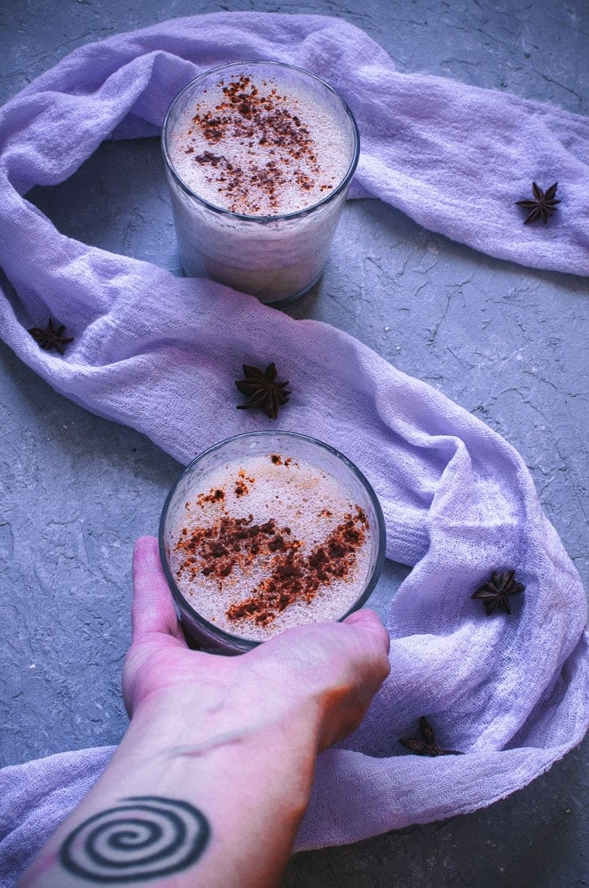 an image of purple cloth on gray background with a hand holding a cup of eggnog