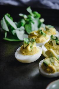 Deviled eggs garnished with dill and avocado slices, accompanied by a side of mixed greens, create an enticing dish perfect for vegetarian keto recipes.