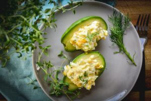 Plate with two avocado halves filled with egg salad, garnished with fresh herbs. A delicious option for those seeking vegetarian keto recipes. Fork and knife are placed beside the plate.