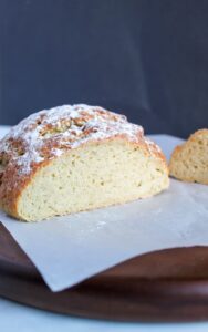 A loaf of bread dusted with flour, partially sliced and placed on a wooden cutting board covered with parchment paper, perfect for those exploring tapioca flour recipes.