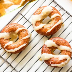 Three pumpkin spice donuts with cream cheese glaze are placed on a cooling rack. The glaze is drizzled over the top of the donuts, creating a tempting treat that's perfect for fans of tapioca flour recipes.