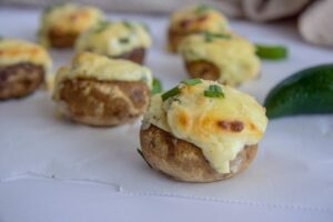Savor these delectable stuffed mushrooms, featured in top vegetarian keto recipes, topped with melted cheese and garnished with chopped green herbs, all beautifully arranged on a white surface.