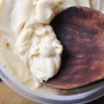 a dark wooden spoon sticking out of a small plastic bowl of white frosting