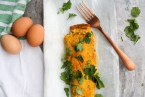 An omelet garnished with cilantro on white parchment paper, accompanied by a copper fork and three brown eggs on the side—a perfect dish for those exploring vegetarian keto recipes.