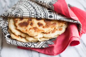 A stack of flatbread, crafted from unique tapioca flour recipes, partially wrapped in a red and black patterned cloth, sits on a marble surface.