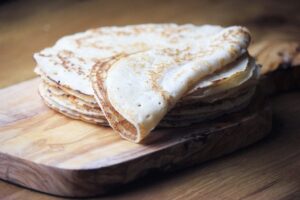 A stack of flat, golden-brown crepes, made from tapioca flour recipes, with one partially folded, sits on a wooden cutting board.