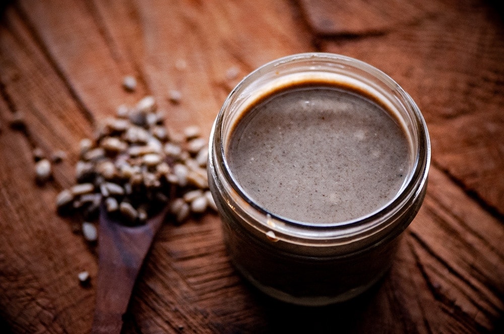 an open jar of sunflower seed butter on a wooden backdrop next to a scatter of sunflower seeds