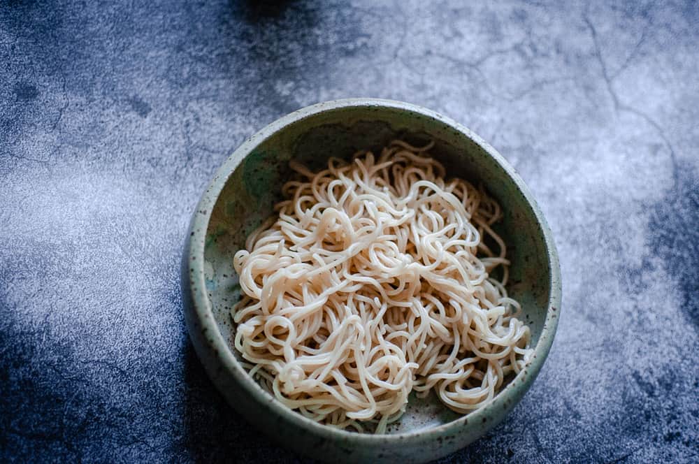 a white bowl of plain ramen noodles on gray background
