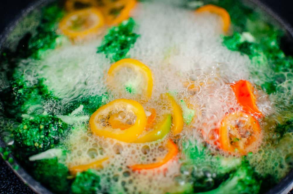 a close up shot of pepper rings and broccoli in boiling water