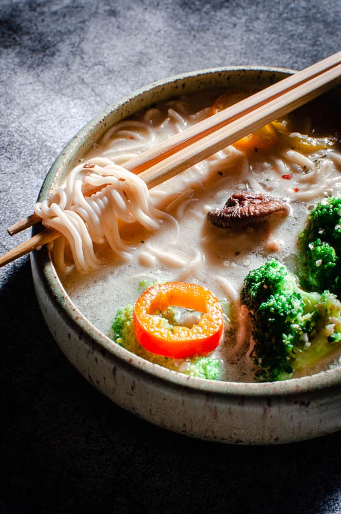 a close up shot of ramen noodles wrapped around chopsticks resting on a bowl