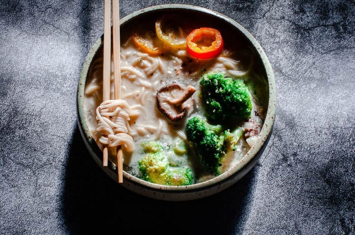 a white bowl filled with ramen noodles lit by sunlight on a gray background