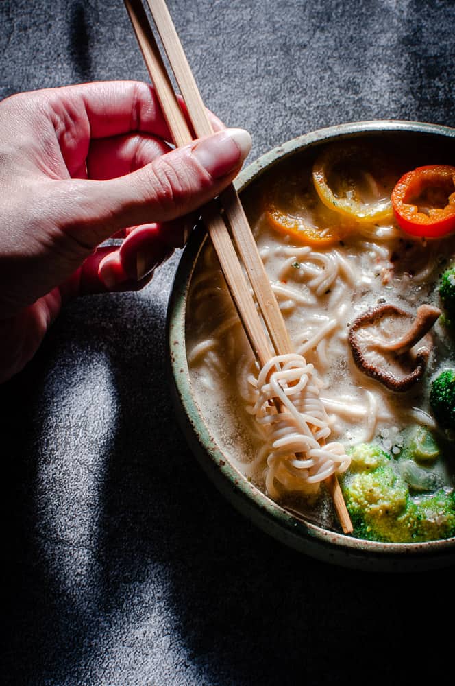 hands holding chopsticks wrapped in vegan ramen noodles