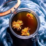 top view of open glass jar filled with mushroom broth topped with calendula flowers