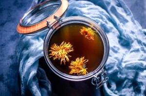 top view of open glass jar filled with mushroom broth topped with calendula flowers