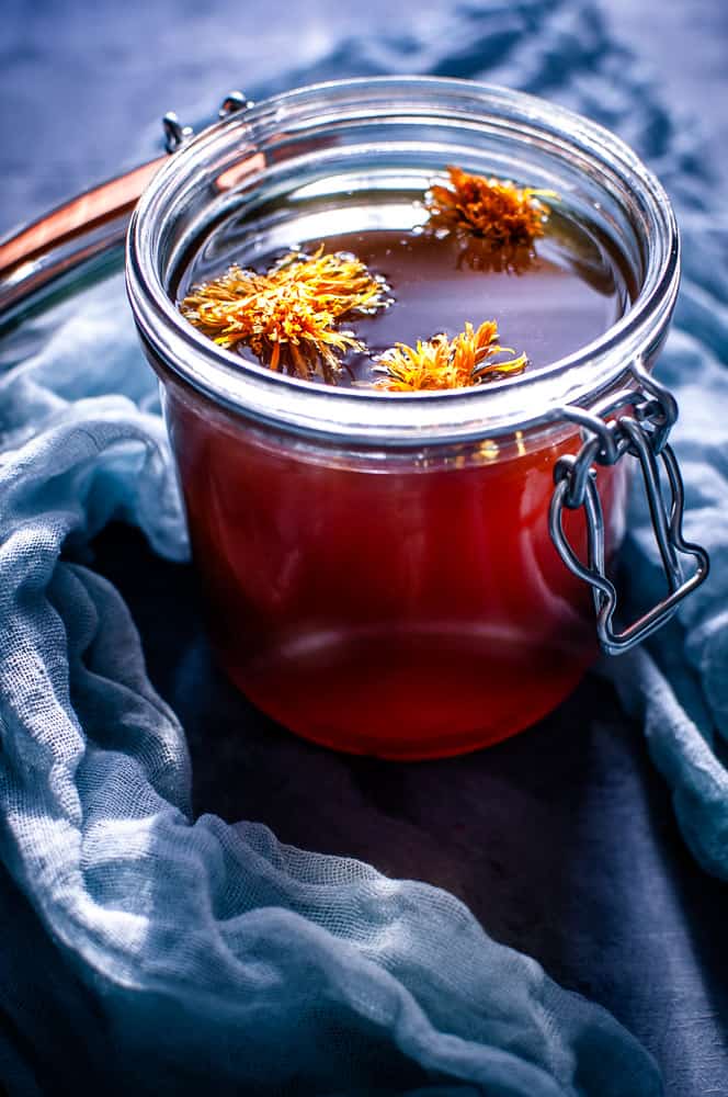 a clear glass jar filled with red vegan mushroom broth topped with calendula flowers