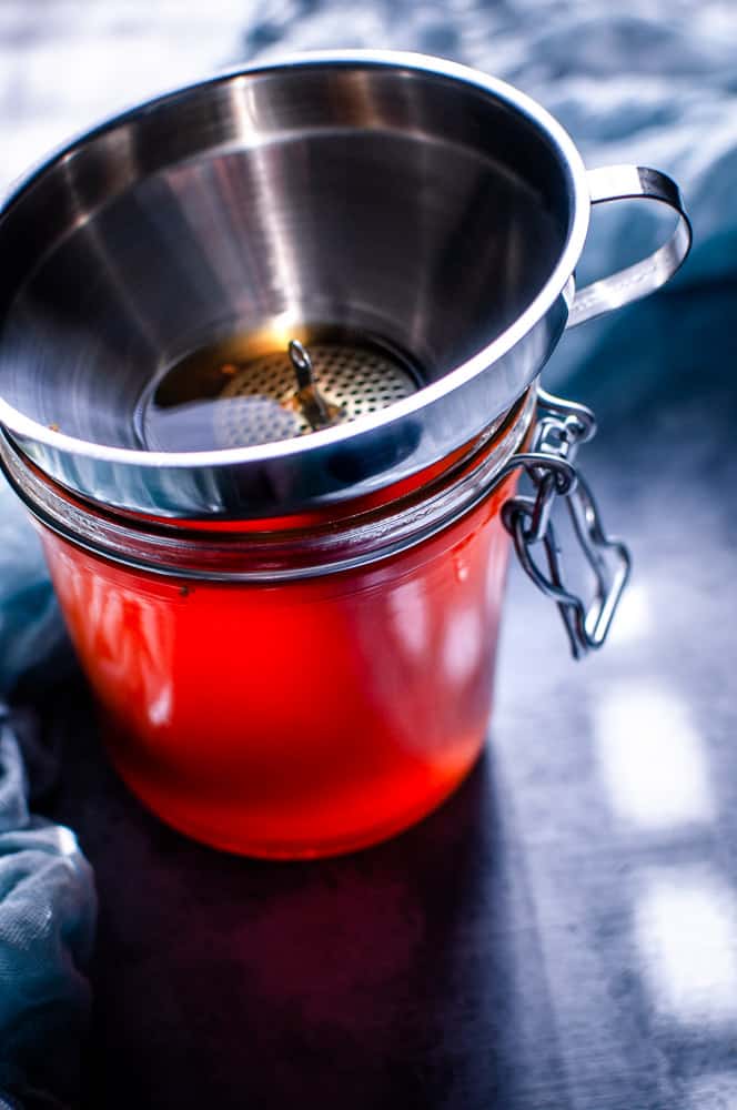 a jar filled with herbal broth with sunlight streaming through making it appear red