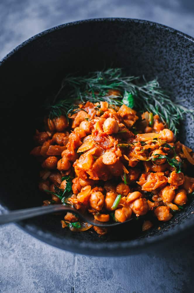 a black bowl filled with harissa chickpeas and a vintage spoon