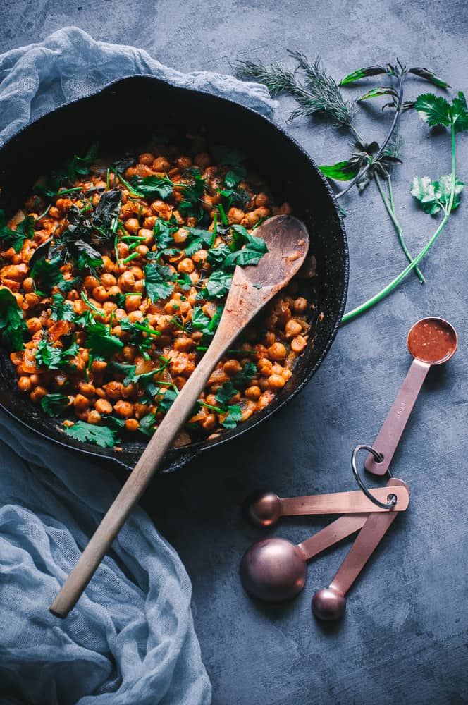 a cast iron skillet filled with orange harissa chickpeas topped with fresh herbs