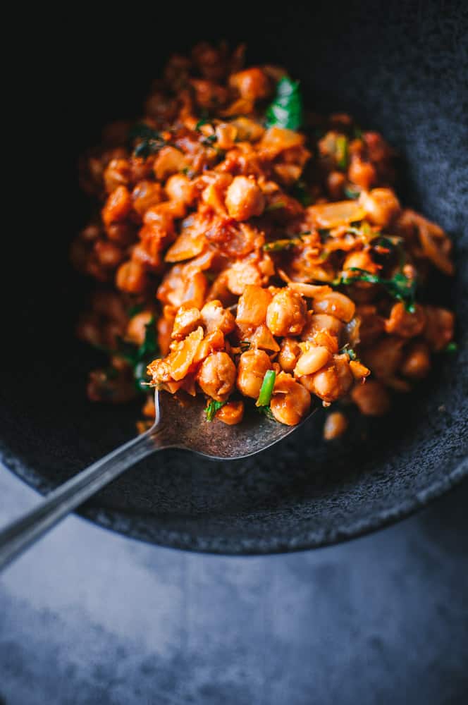 a close up of harissa chickpeas in black bowl with vintage spoon