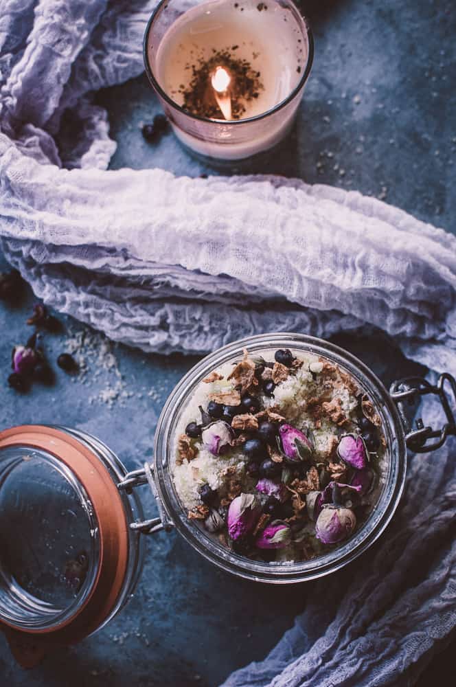 a lit candle with a purple cheesecloth and open jar of bath soak