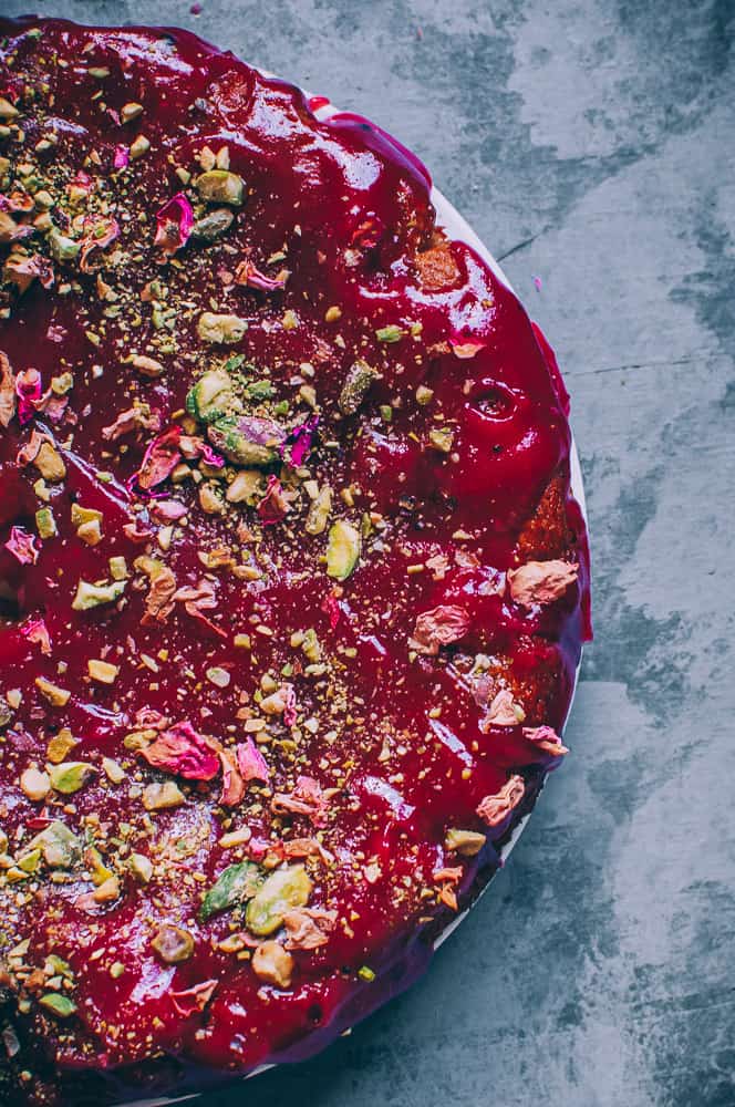 top view red cake topped with crushed pistachios and rose petals