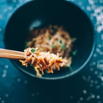 a hand holding chopsticks wrapped in spicy sesame noodles