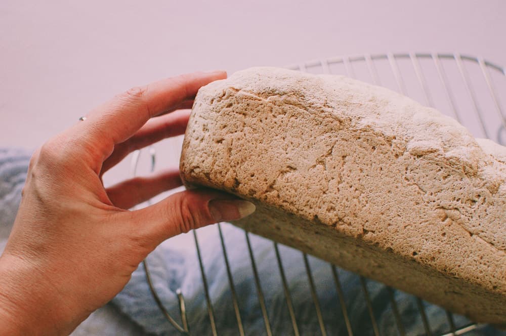 a hand holding a fresh loaf of vegan gluten free bread