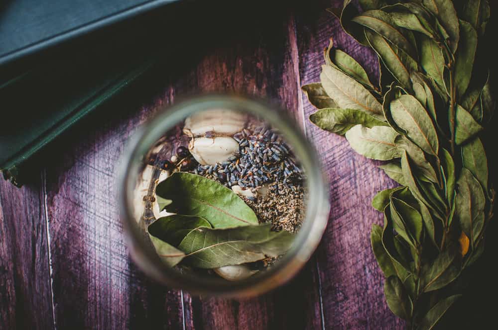 a jar filled with bay leaves lavender and garlic cloves on a wooden background