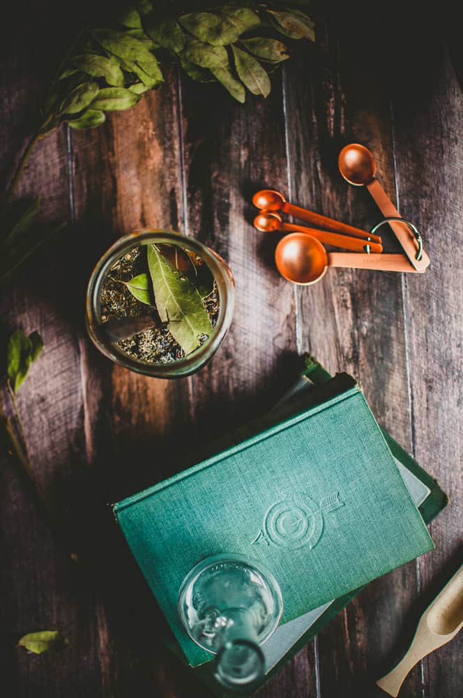 a stack of vintage books, measuring spoons and  jar with bay leaves