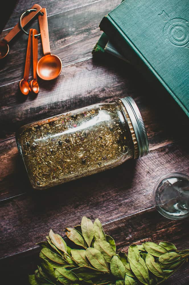 a jar filled with four thieves vinegar alongside measuring spoons books and bay leaves