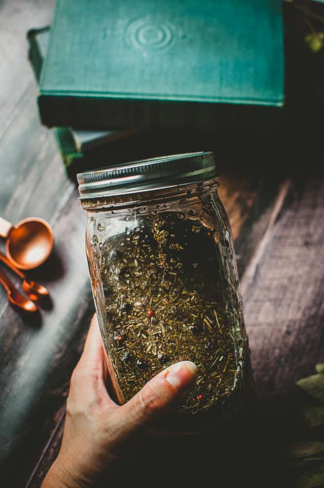 a hand holding a jar filled with vinegar and herbs