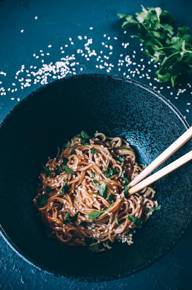 black ceramic bowl filled with sesame ramen noodles chopsticks cilantro