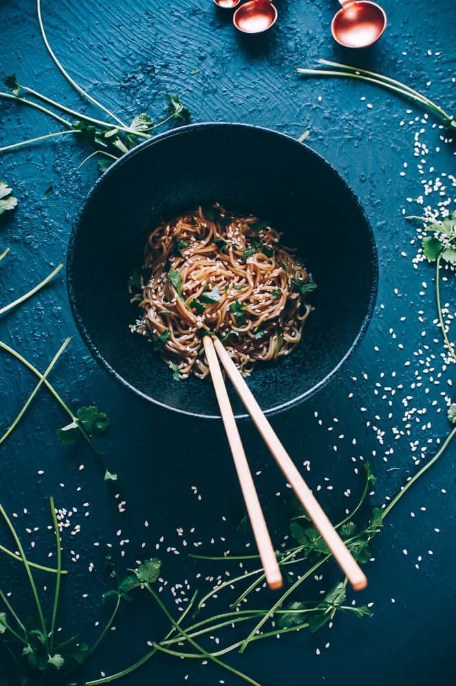 flatlay black bowl sesame noodles chopsticks cilantro measuring spoons sesame seeds
