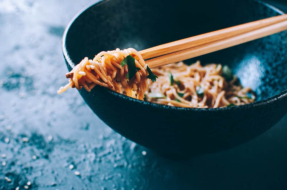 chopsticks wrapped with ramen noodles resting on side of bowl