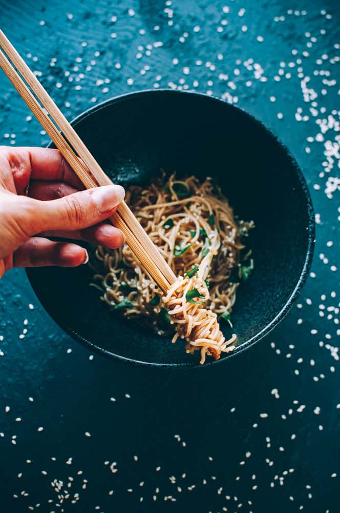 hand holding chopsticks over bowl filled with sesame noodles