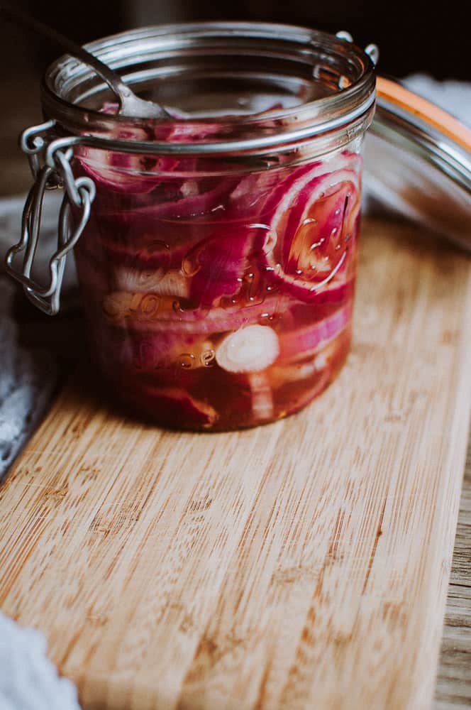 a cutting board with a jar of pickled onions sitting on it