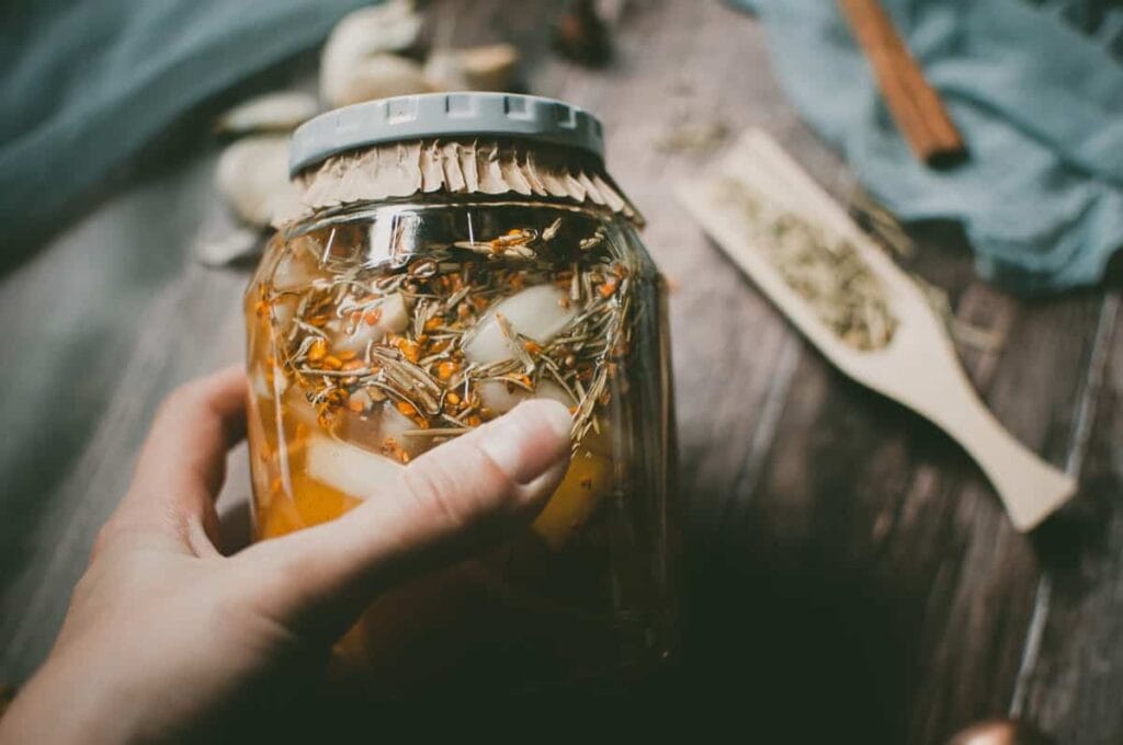 a hand holding a jar filled with vinegar and herbs