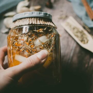 a hand holding a jar filled with vinegar and herbs