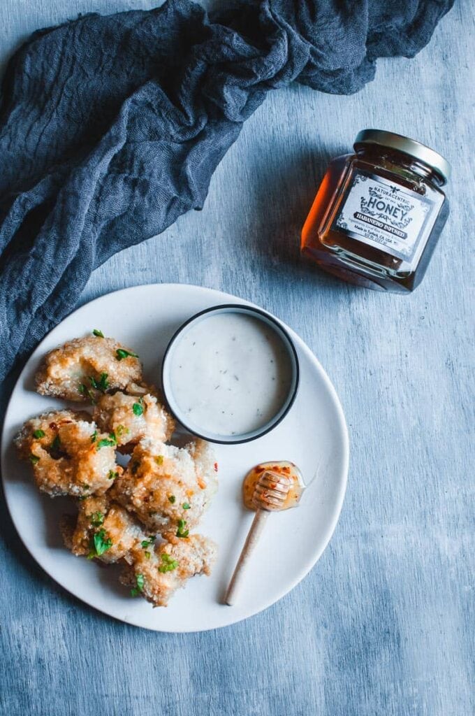 a flatlay with white plate topped with cauliflower wings and honey