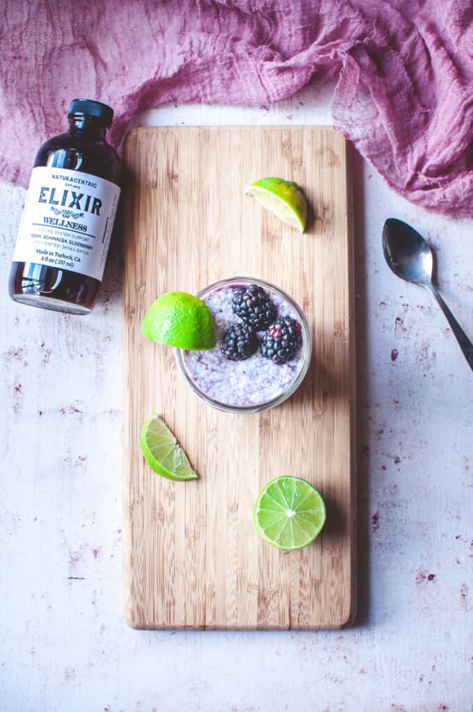 top view shot of a cutting board with a glass of chia parfit sitting on it garnished with lime wedges and blackberries