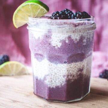 a jar filled with chia seed pudding and purple smoothie garnished with lime and blackberries