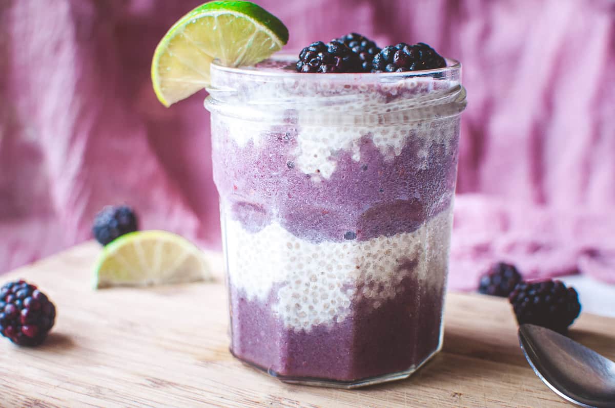 a jar filled with chia seed pudding and purple smoothie garnished with lime and blackberries
