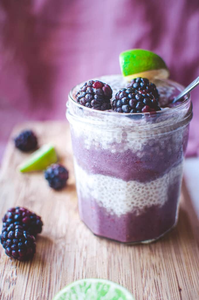 a glass filled with purple smoothie layers and chia seed pudding