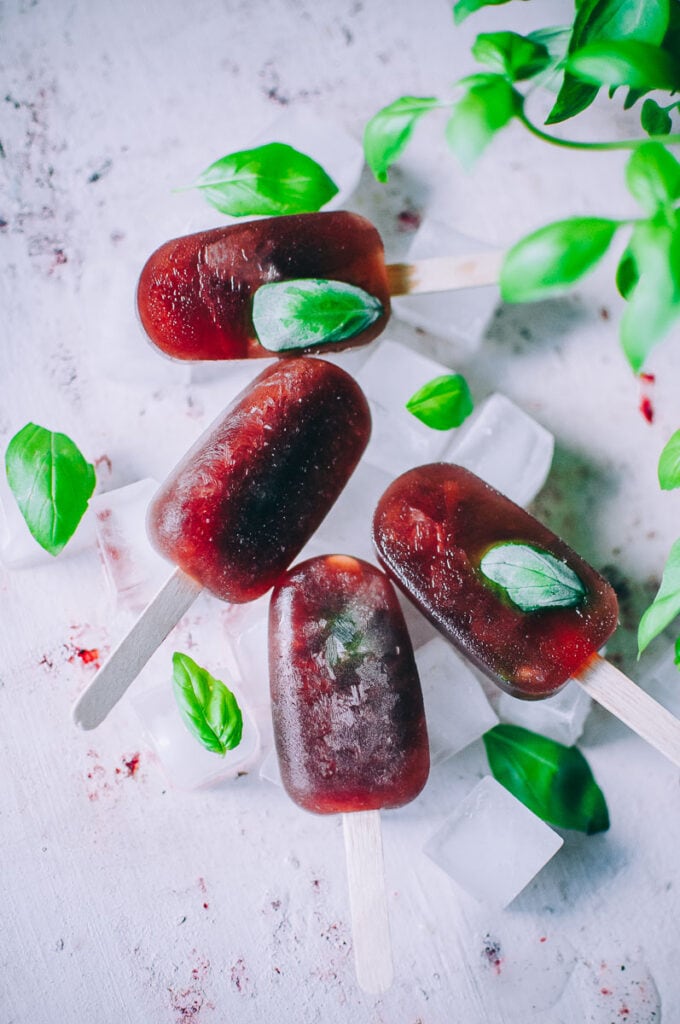 ruby red popsicles scattered with basil leaves