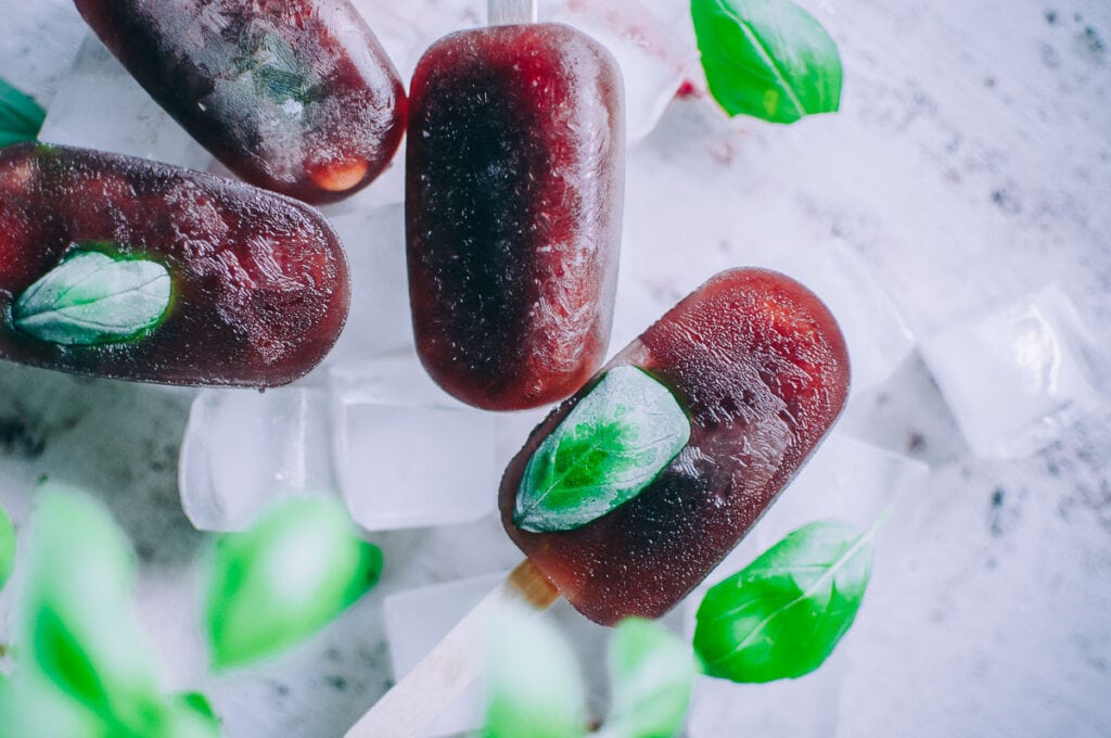 red popsicles with basil leaves sitting on a bed of ice