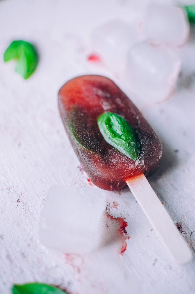 a red popsicle on a pink backdrop dotted with basil leaves