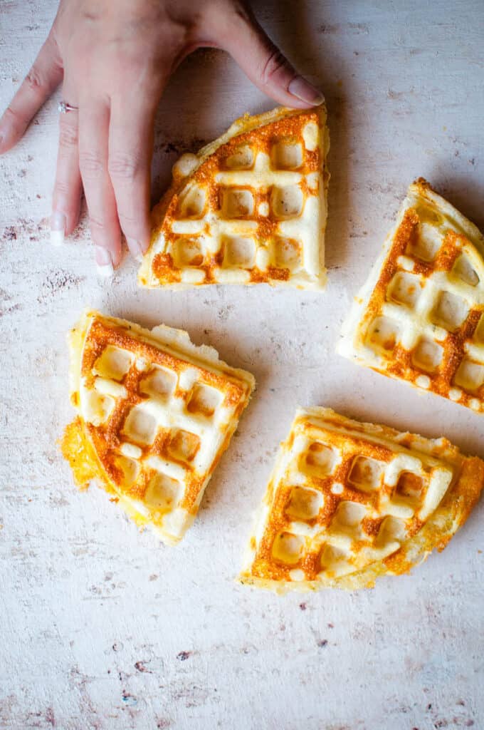 4 cheesy waffles with a hand reaching for them