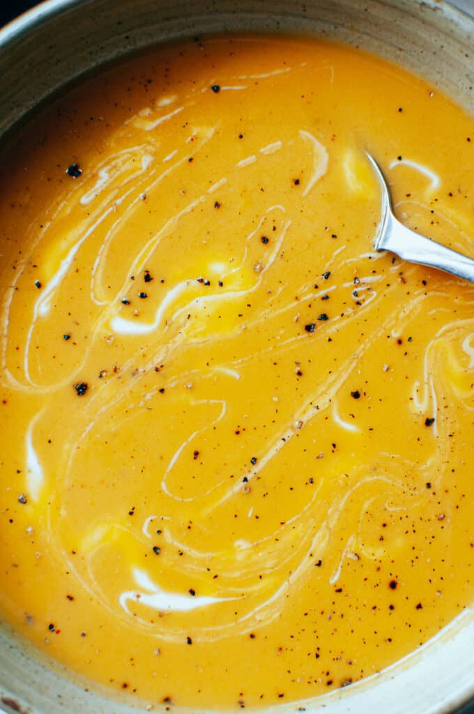 a close shot of a swirl of yogurt and a sprinkle of black pepper in a bowl of orange soup